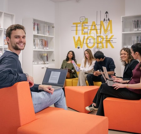 Espace coworking orange moderne, équipe en collaboration avec ordinateurs et bibliothèque.