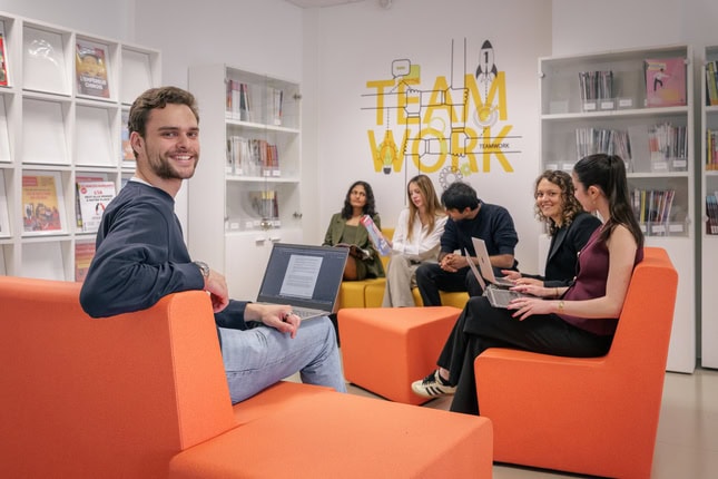 Espace coworking orange moderne, équipe en collaboration avec ordinateurs et bibliothèque.
