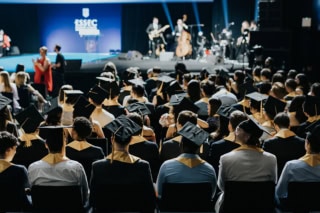 Cérémonie ESSEC remise de diplômes 2026 : étudiants en toques et écharpes dorées, scène musicale.