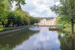 Étang paisible avec manoir, reflets, fontaine et arbres dans un parc formel.