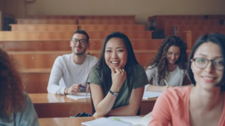 Étudiante souriante prenant des notes en cours dans un amphithéâtre universitaire.