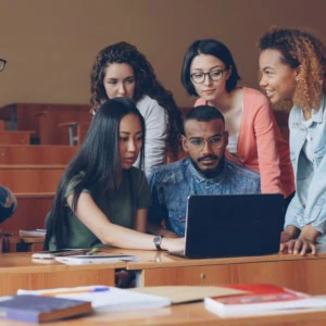 Étudiants en groupe autour dun ordinateur portable en amphithéâtre pour projet collaboratif.