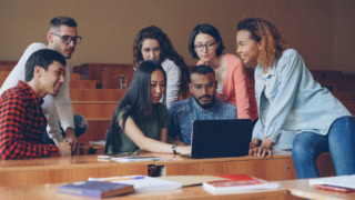 Étudiants en groupe autour dun ordinateur portable en amphithéâtre pour projet collaboratif.
