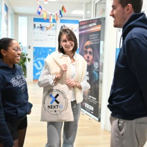Étudiants en conversation dans un couloir de campus décoré de drapeaux internationaux.
