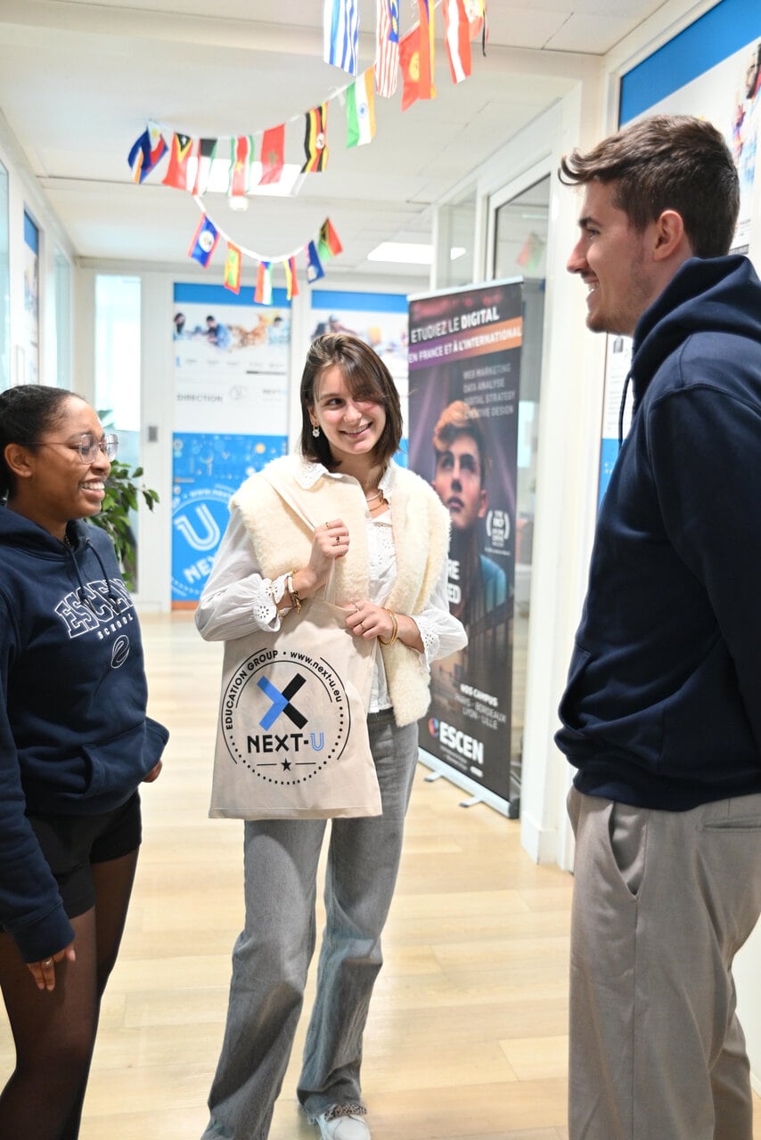 Étudiants en conversation dans un couloir de campus décoré de drapeaux internationaux.
