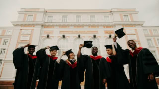 Étudiants diplômés lancent leurs birets devant un bâtiment universitaire historique.