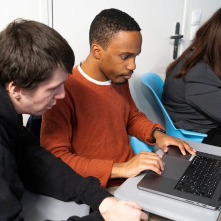Étudiants concentrés sur ordinateurs portables en classe, collaboration et apprentissage numérique.