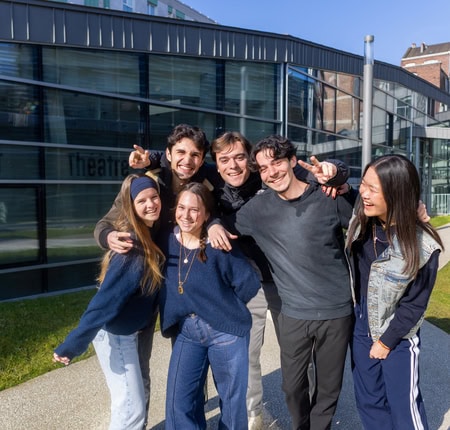 Groupe damis urbain au soleil, jeunes adultes souriants devant théâtre moderne.