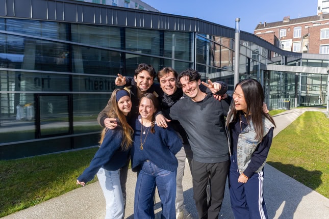 Groupe damis urbain au soleil, jeunes adultes souriants devant théâtre moderne.