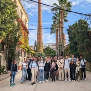 Groupe de jeunes dans une cour végétalisée devant cheminée en brique et palmiers.