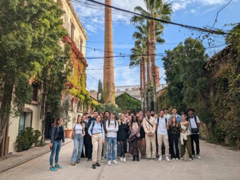 Groupe de jeunes dans une cour végétalisée devant cheminée en brique et palmiers.