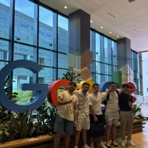 Groupe de jeunes devant logo Google coloré dans le lobby lumineux dun bureau moderne.