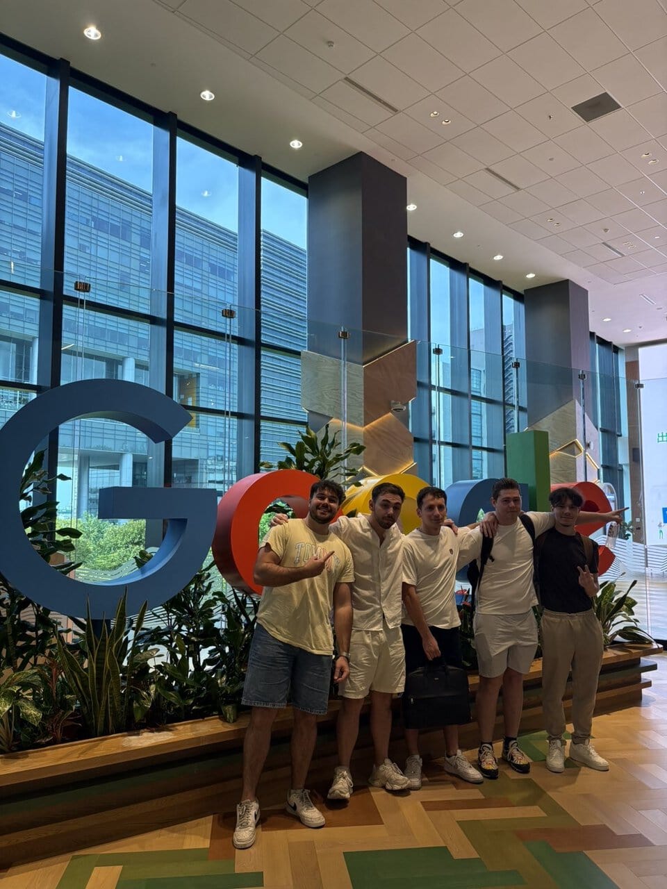 Groupe de jeunes devant logo Google coloré dans le lobby lumineux dun bureau moderne.