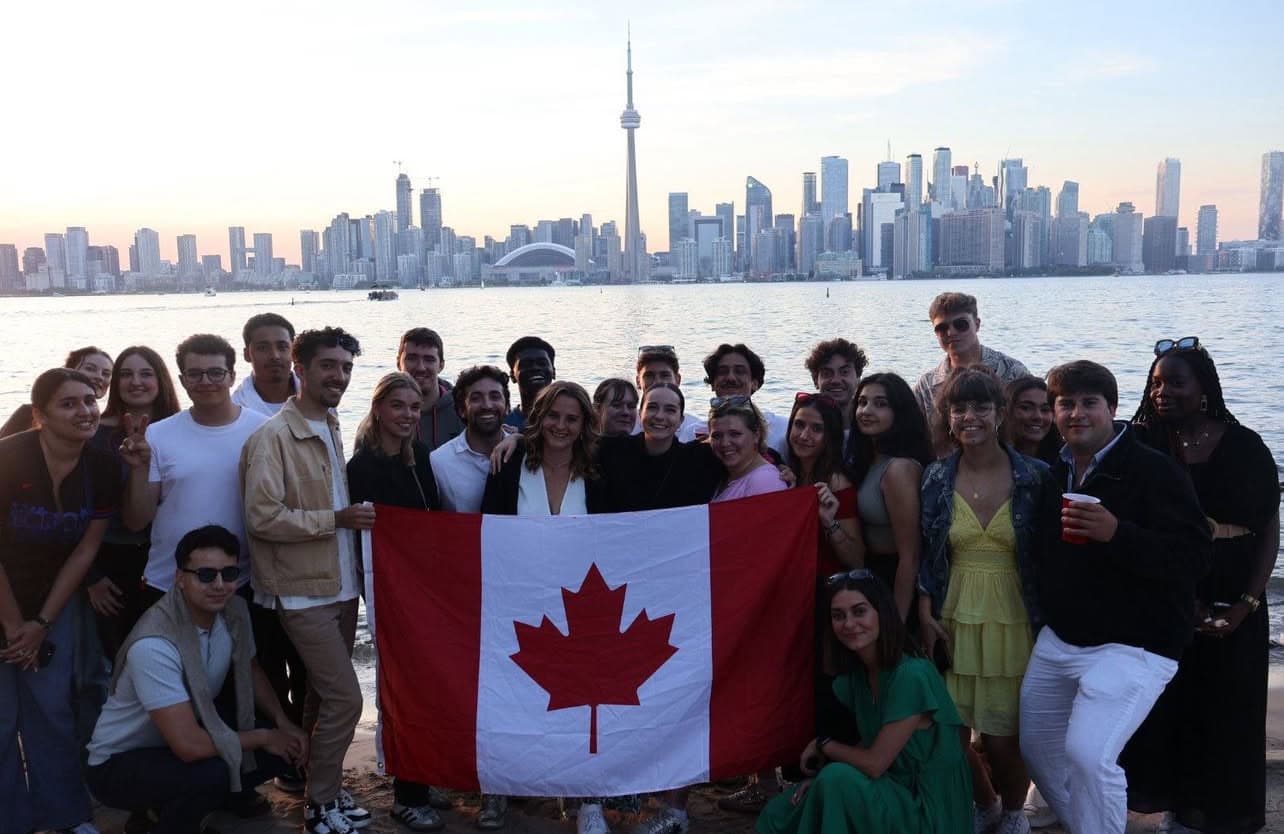 Groupe damis brandissant drapeau canadien devant la skyline de Toronto au bord de leau.