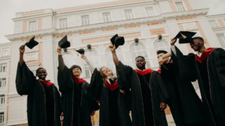 Étudiants diplômés lançant leurs toques devant un bâtiment universitaire classique.