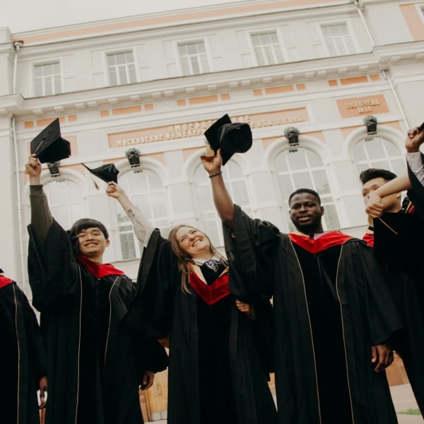 Étudiants diplômés lançant leurs toques devant un bâtiment universitaire classique.