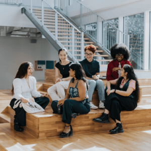 Groupe détudiants en discussion dans un espace de réunion intérieur moderne avec gradins en bois.
