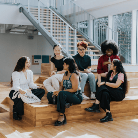 Groupe détudiants en discussion dans un espace de réunion intérieur moderne avec gradins en bois.