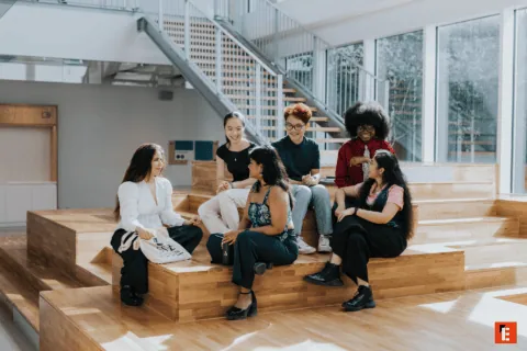 Groupe détudiants en discussion dans un espace de réunion intérieur moderne avec gradins en bois.