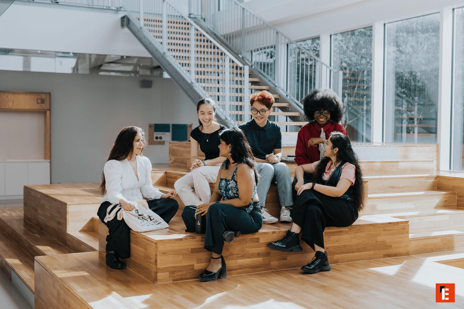 Groupe détudiants en discussion dans un espace de réunion intérieur moderne avec gradins en bois.