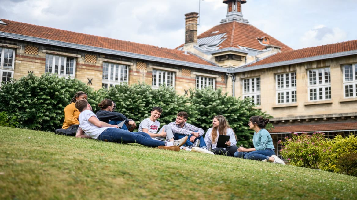 Groupe détudiants sur pelouse de campus discutant et travaillant en extérieur.