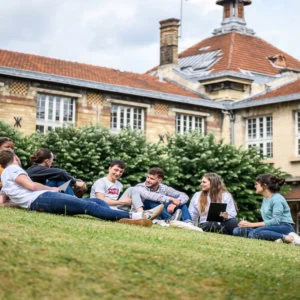 Groupe détudiants sur pelouse de campus discutant et travaillant en extérieur.