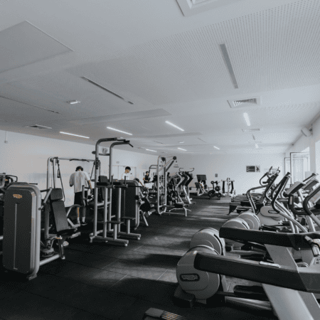Salle de sport moderne lumineuse avec appareils cardio, machines de musculation et tapis de course.