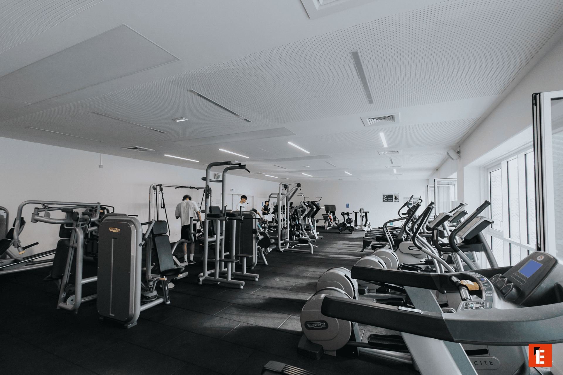 Salle de sport moderne lumineuse avec appareils cardio, machines de musculation et tapis de course.