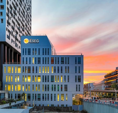 Bâtiment IÉSEG sur campus moderne au coucher de soleil, façade vitrée et passerelle piétonne.