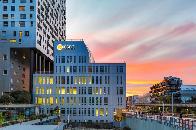 Bâtiment IÉSEG sur campus moderne au coucher de soleil, façade vitrée et passerelle piétonne.