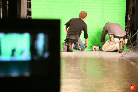Techniciens installant un écran vert sur le plateau de tournage en studio.