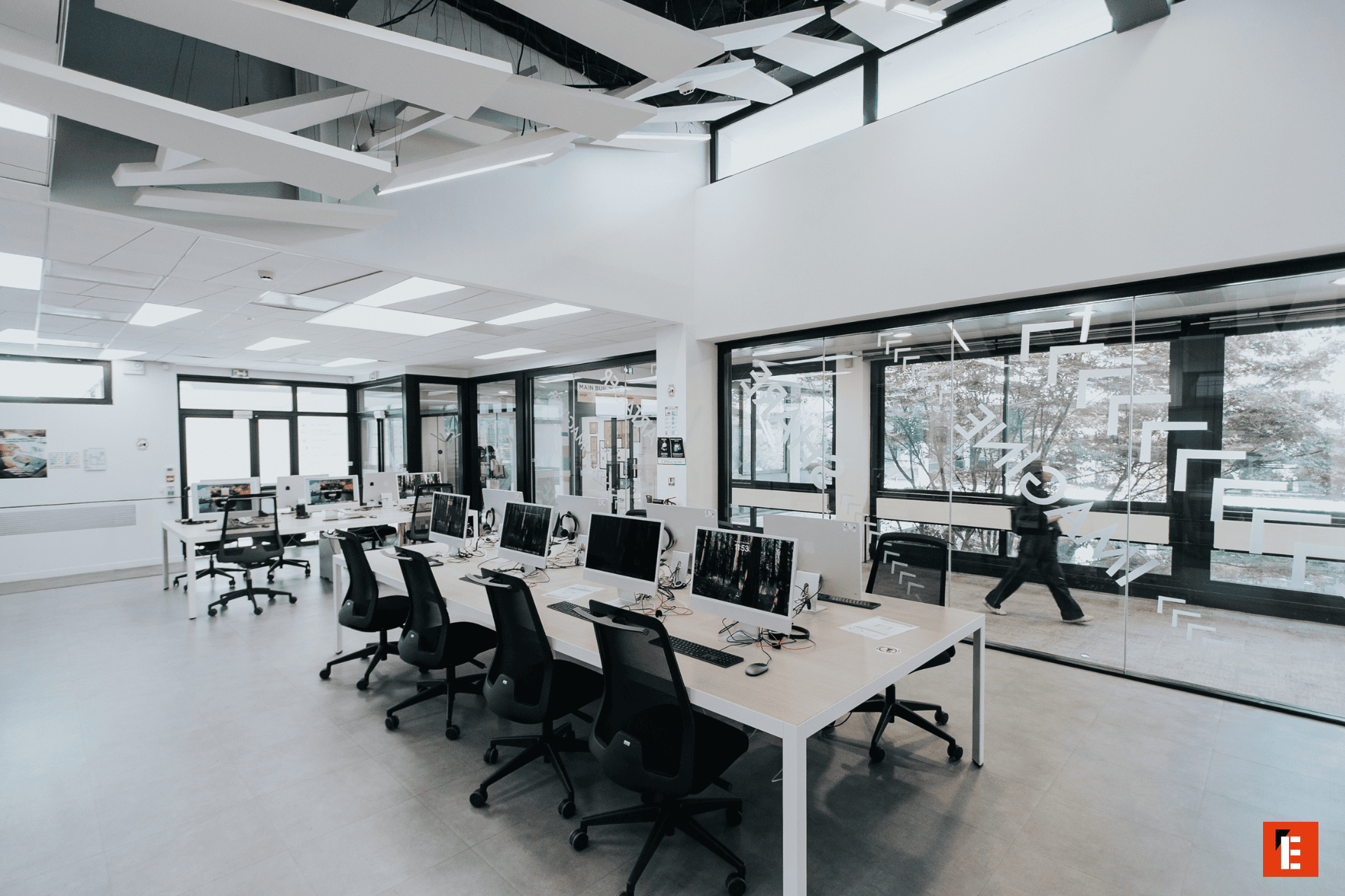 Laboratoire informatique lumineux moderne avec rangées dordinateurs, postes de travail ergonomiques et cloisons vitrées.