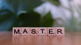 Tuiles en bois «MASTER» style Scrabble sur surface réfléchissante, flou artistique en arrière-plan.