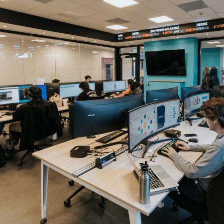 Open space bureau informatique avec rangées dordinateurs, écrans incurvés et postes de travail collaboratifs.