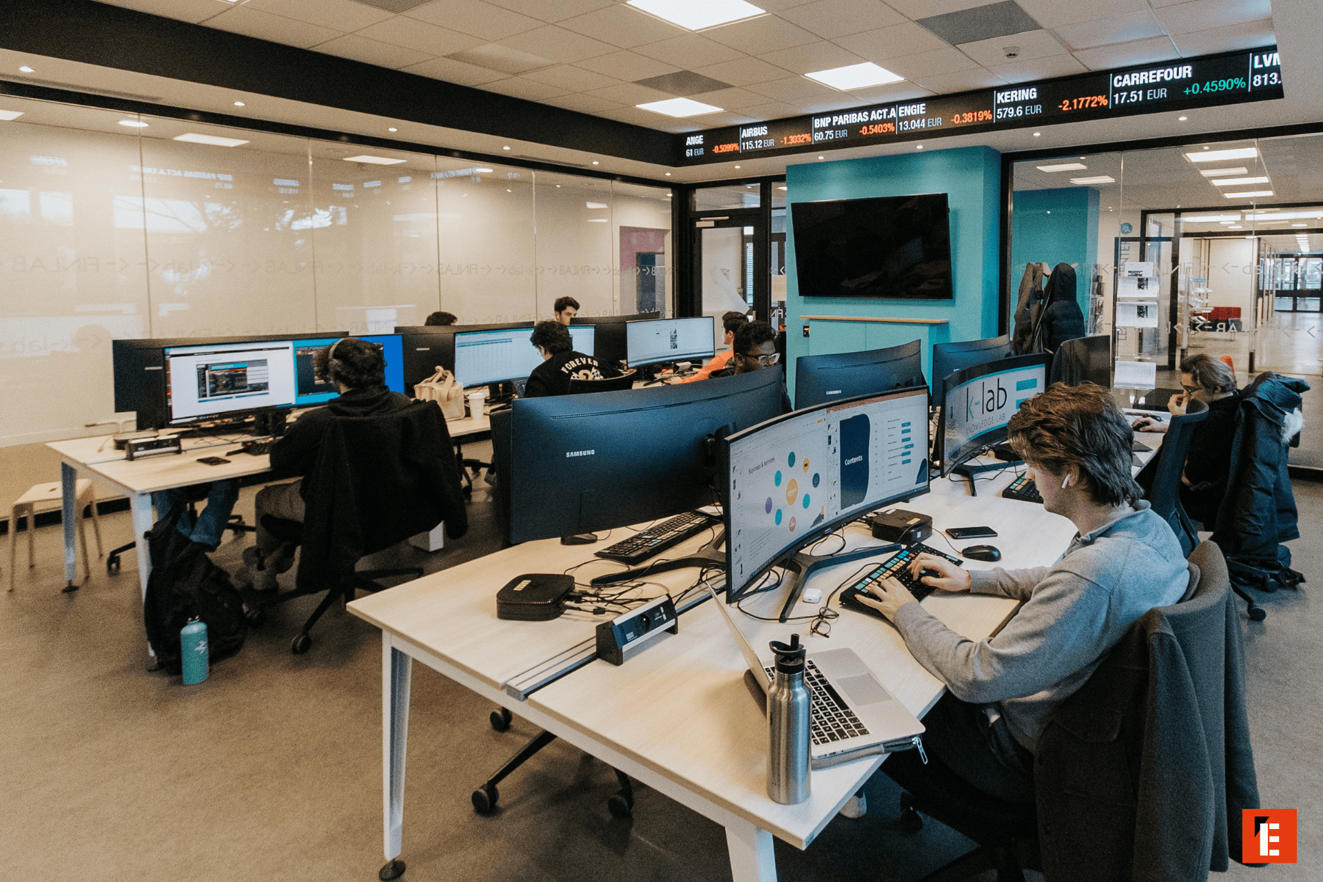 Open space bureau informatique avec rangées dordinateurs, écrans incurvés et postes de travail collaboratifs.