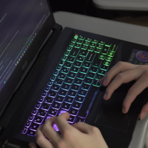 Ordinateur portable MSI avec clavier RGB, écran de code et mains en train de taper.