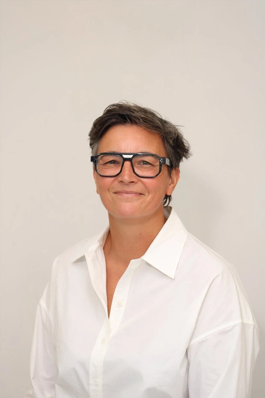 Portrait professionnel en studio : personne cheveux courts, lunettes, chemise blanche, sourire naturel.