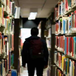 Allée de bibliothèque bordée de rayonnages remplis de livres, silhouette détudiant au loin.