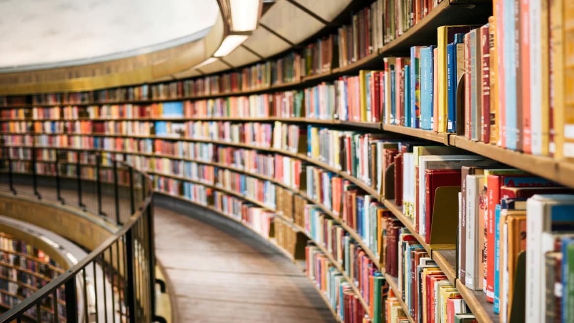 Salle de lecture circulaire, rayonnages courbes en bois et étagères remplies de livres.