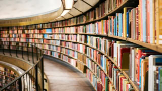 Salle de lecture circulaire, rayonnages courbes en bois et étagères remplies de livres.