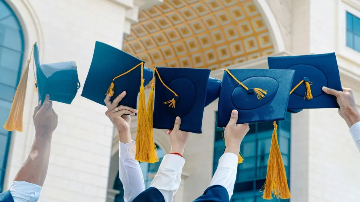 Remise de diplômes à luniversité, chapeaux bleu marine levés devant bâtiment classique.