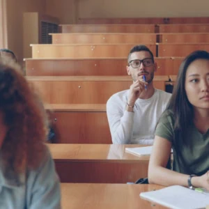 Salle de cours en bois, lumière naturelle, étudiants concentrés prenant des notes.