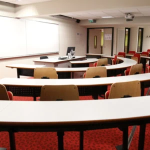 Salle de cours semi-circulaire moderne, amphithéâtre avec pupitres, estrade, projecteur.