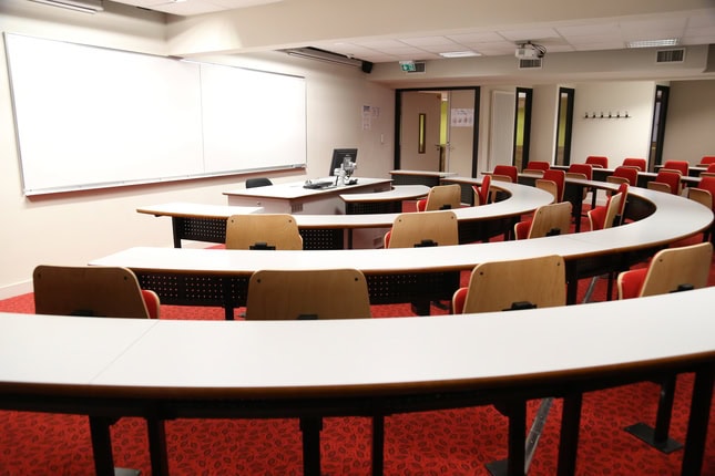 Salle de cours semi-circulaire moderne, amphithéâtre avec pupitres, estrade, projecteur.