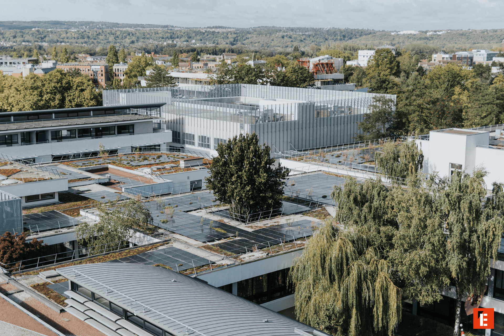 Toits avec panneaux solaires et végétalisés sur campus urbain moderne, bâtiments et arbres.