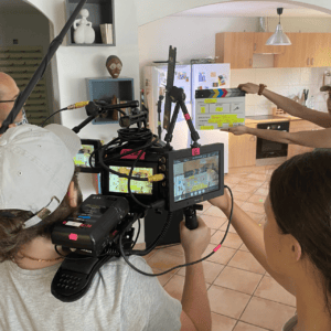 Tournage en cuisine : équipe technique entourant caméra épaulée et clap prêt.