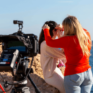 Tournage plage : caméra sur rochers, équipe coiffure préparant actrice devant mer.