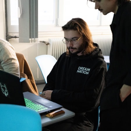 Trois personnes aux bureaux, ordinateurs portables, travail collaboratif et concentration.