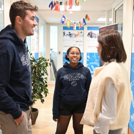 Trois étudiants discutent dans un couloir lumineux détablissement universitaire.