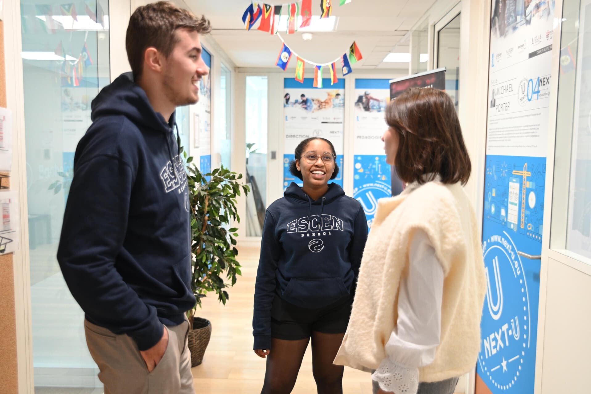 Trois étudiants discutent dans un couloir lumineux détablissement universitaire.